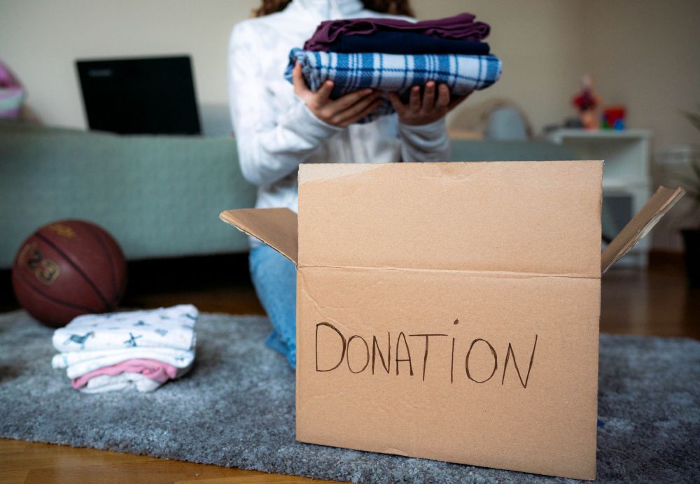 A woman holds clothes over a donation box.