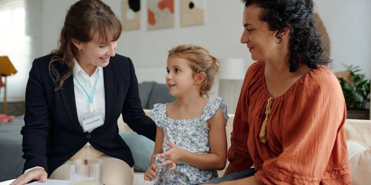 A CTA team member sits on a couch and engages with a young girl while her mother sits next to her.