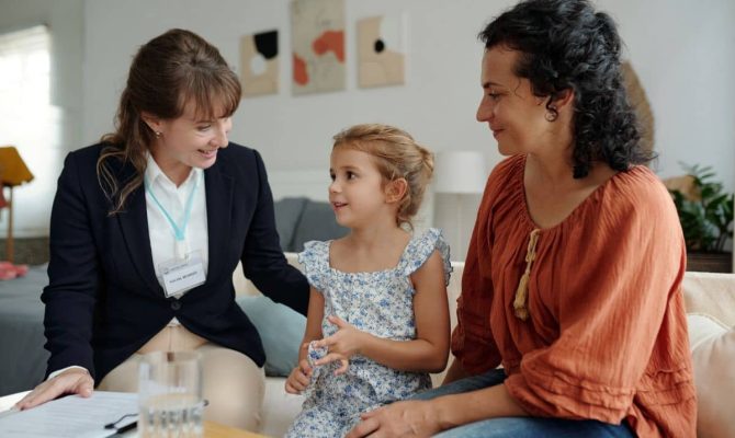 A CTA team member sits on a couch and engages with a young girl while her mother sits next to her.