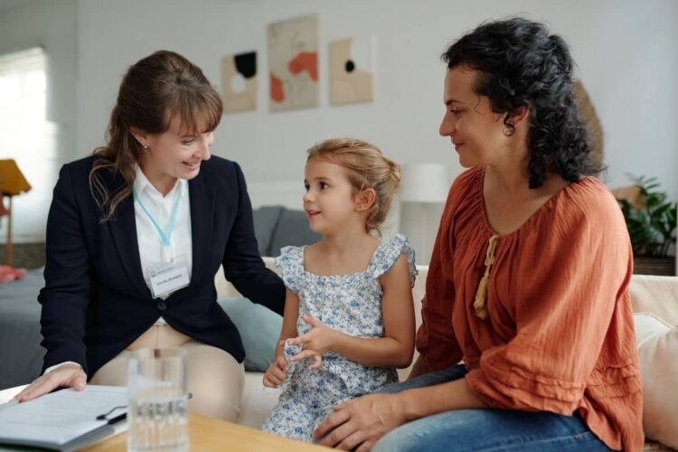 An in-home visit from a female therapist, a little girl, and her mother in a living room.