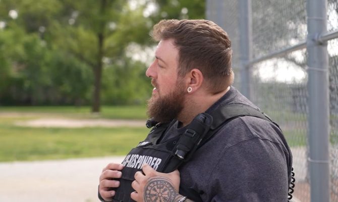 Peer Co-Responder John looks out of the frame while holding his hands tucked in a bullet-proof vest.