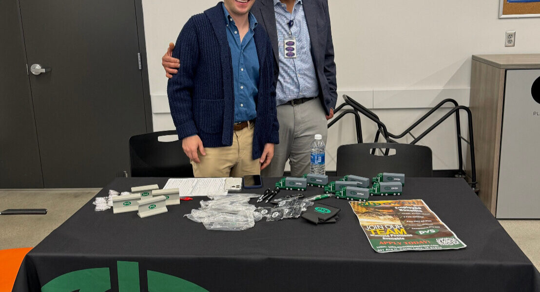 Abbas Alodan and a representative from Owen stand in front of a table at a Refugee Career Fair held at Lutheran Family Services.