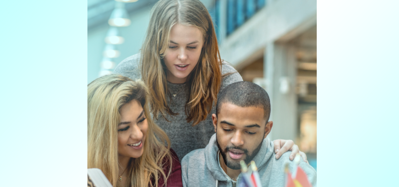 A young woman looks over the shoulders of two studying students to read a book.