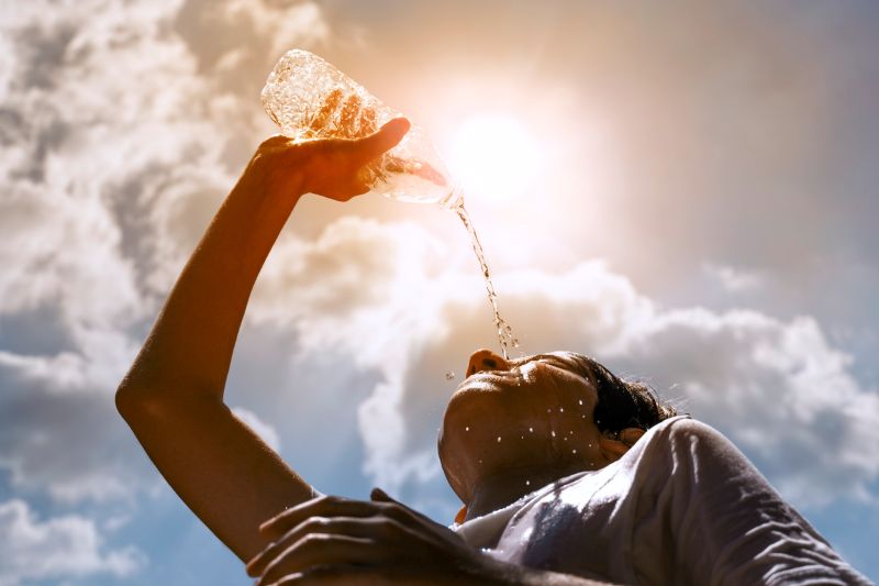 A boy dumps water on his head as a scorching sun looms overhead.