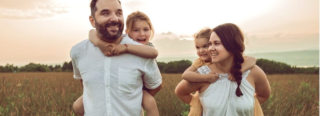 A smiling family walks through a field at sunset.