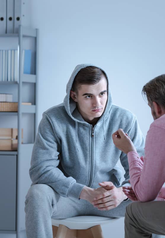 A teen wearing a gray hoodie receives counseling for substance use.