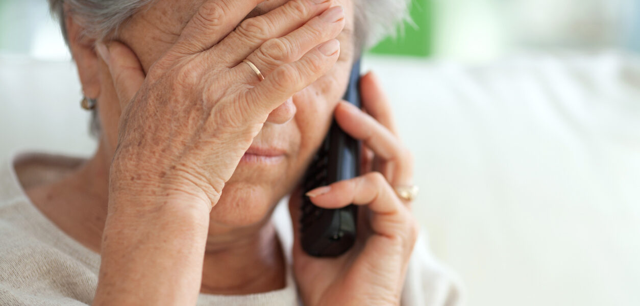 A woman covers her forehead with her hand as she holds a telephone to her ear.