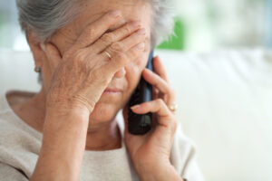 A woman covers her forehead with her hand while holding a telephone to her ear.