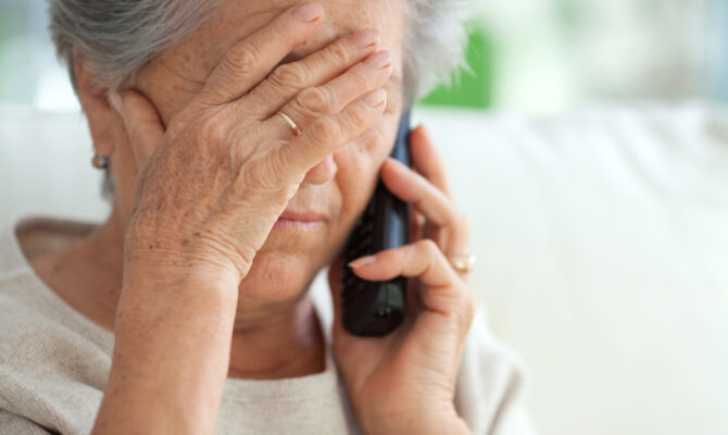 A woman covers her forehead with her hand as she holds a telephone to her ear.
