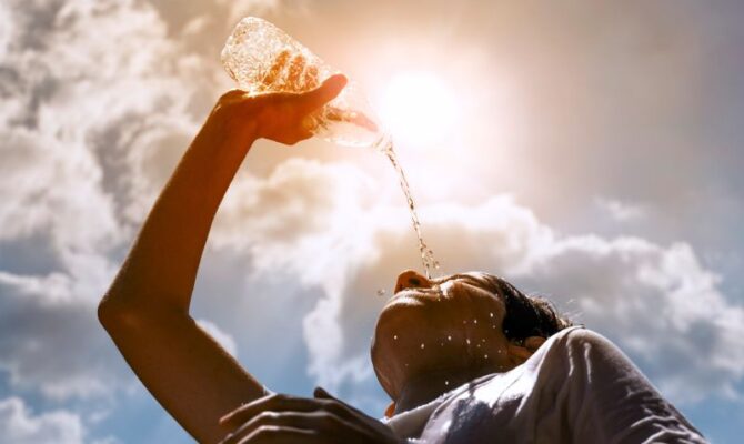 A boy dumps water on his head as a scorching sun looms overhead.