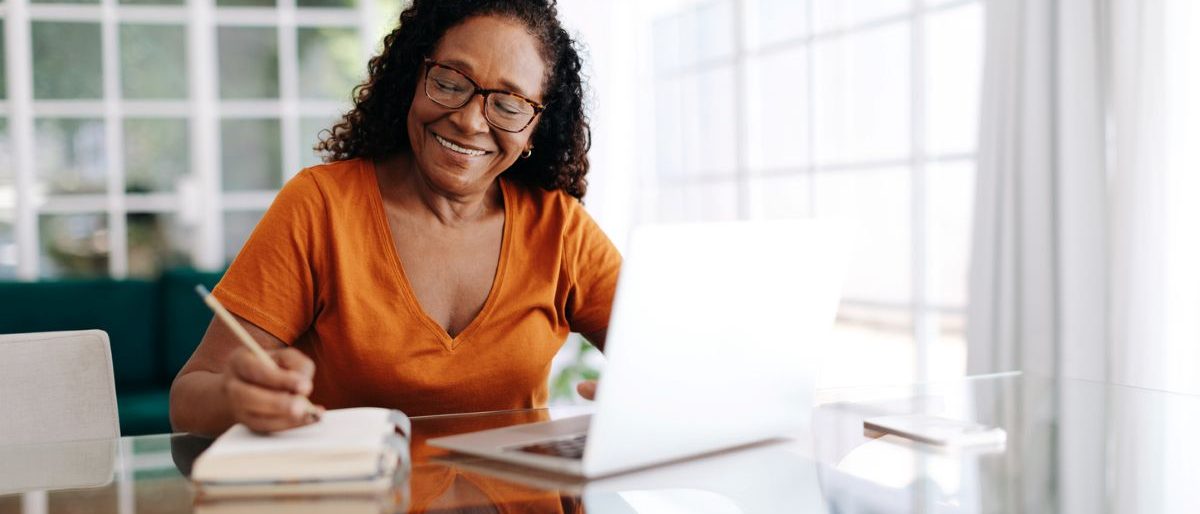A woman makes her will at a computer while taking notes on a notepad.