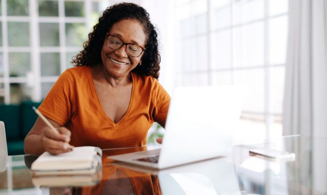 A woman makes her will at a computer while taking notes on a notepad.